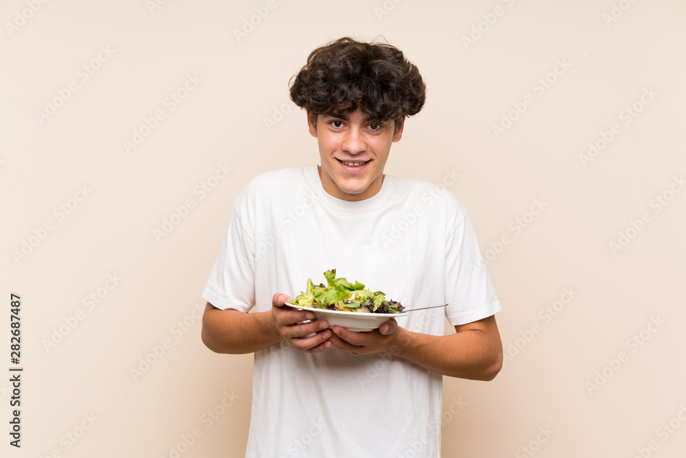 Young man with salad over isolated green wall Young man with salad over isolated green wall