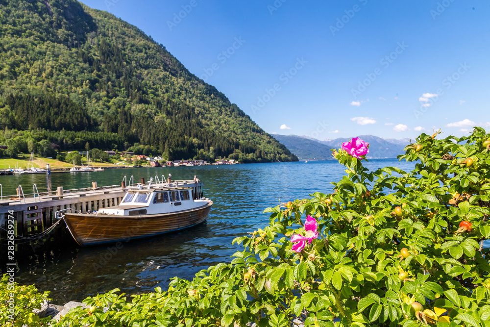 Norwegian panorama with mountains surrounding a fjord in Norway, boat and pink flowers. View from habour of Vik, a town along Sognefjord in Norway