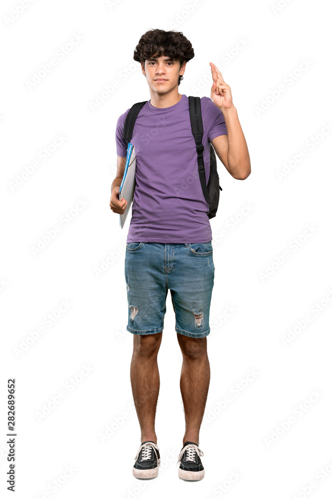 A full-length shot of a Young student man with fingers crossing and wishing the best over isolated white background A full-length shot of a Young student man with fingers crossing and wishing the best over isolated white background