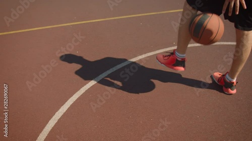 Closeup portrait of male basketball player successfully throwing a ball in hoop on the court with shadow on the ground outdoors with bridge on the background