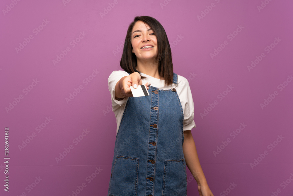 Young Mexican woman over isolated background holding a credit card Young Mexican woman over isolated background holding a credit card
