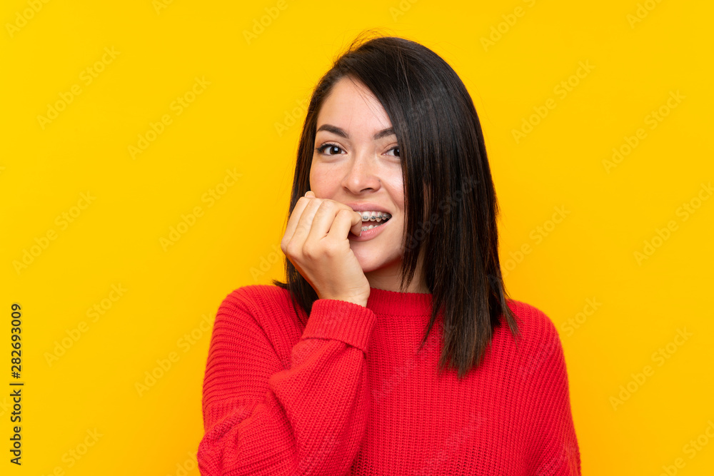 Young Mexican woman with red sweater over yellow wall nervous and scared Young Mexican woman with red sweater over yellow wall nervous and scared