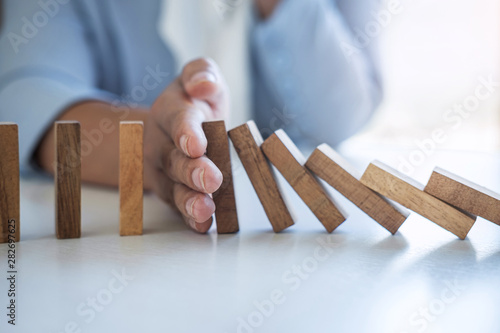 Risk and Strategy in Business, Image of hand stopping falling collapse wooden block dominoes effect from continuous toppled block, prevention and development to stability photo