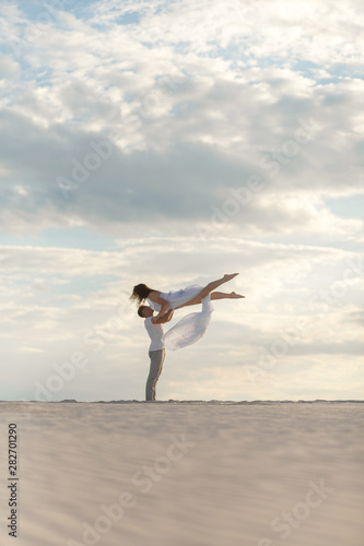 Romantic couple dancing in sand desert. The guy lifts the girl above himself. Sunset sky