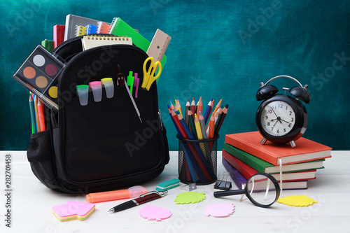 Back to school concept. School bag, pencils, crayons, scissor, notebooks, alarm clock, eraser, markers, watermark, ruler, pencil sharpener, magnifying glass in a combine with a cyan background