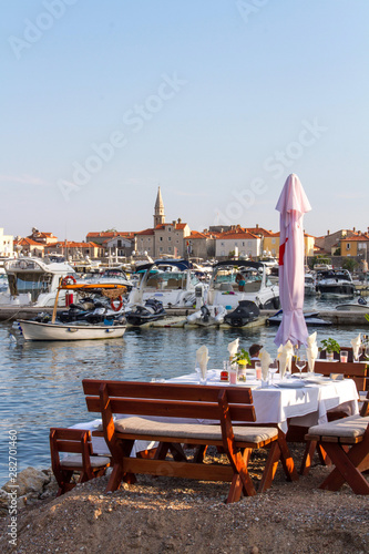 Budva, Montenegro. Restaurant table on the seashore, yacht marina and the old town. 