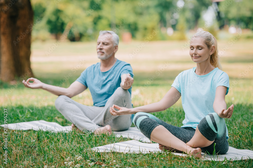 mature man and woman meditating in lotus poses while sitting on yoga mats