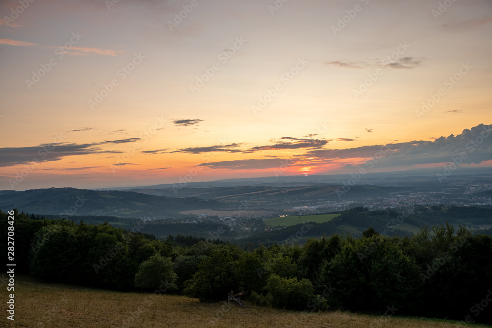 Sunset with view on landscape with fully colored clouds orange and purple and sun behind it and city Valasske Mezirici captured during summer late time.