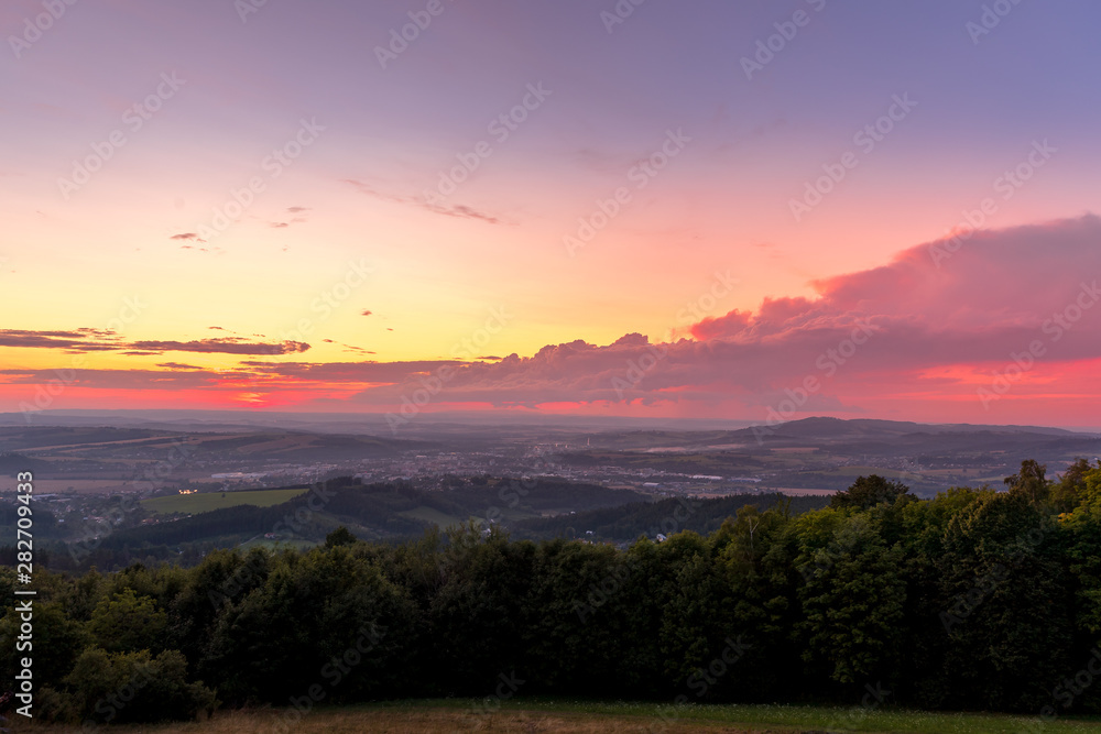Landscape sunset with fully colored clouds pink orange sky look on meadow close to city Valasske Mezirici captured during summer late time.
