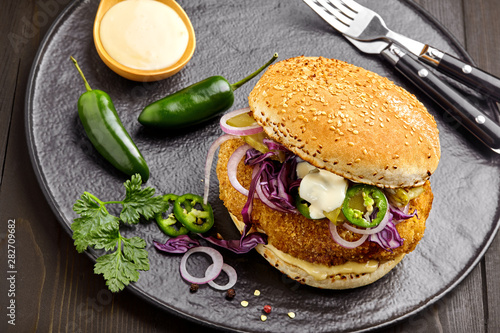 Delicious chicken burger with red onion, pickled cucumber, jalapeno and mayonnaise on a black plate. Classic American food. Top view, directly above shot.