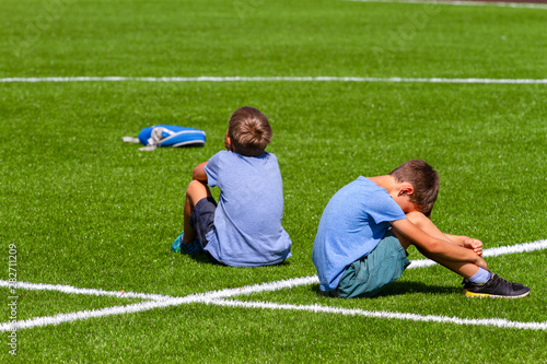 Two sad disappointed boys sitting back to back on the grass in stadium