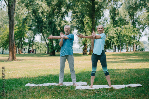 positive, mature man and woman practicing yoga while standing on yoga mats in park © LIGHTFIELD STUDIOS