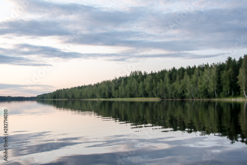 Panorama of the lake shore at sunset with reflection in the water. Finland .