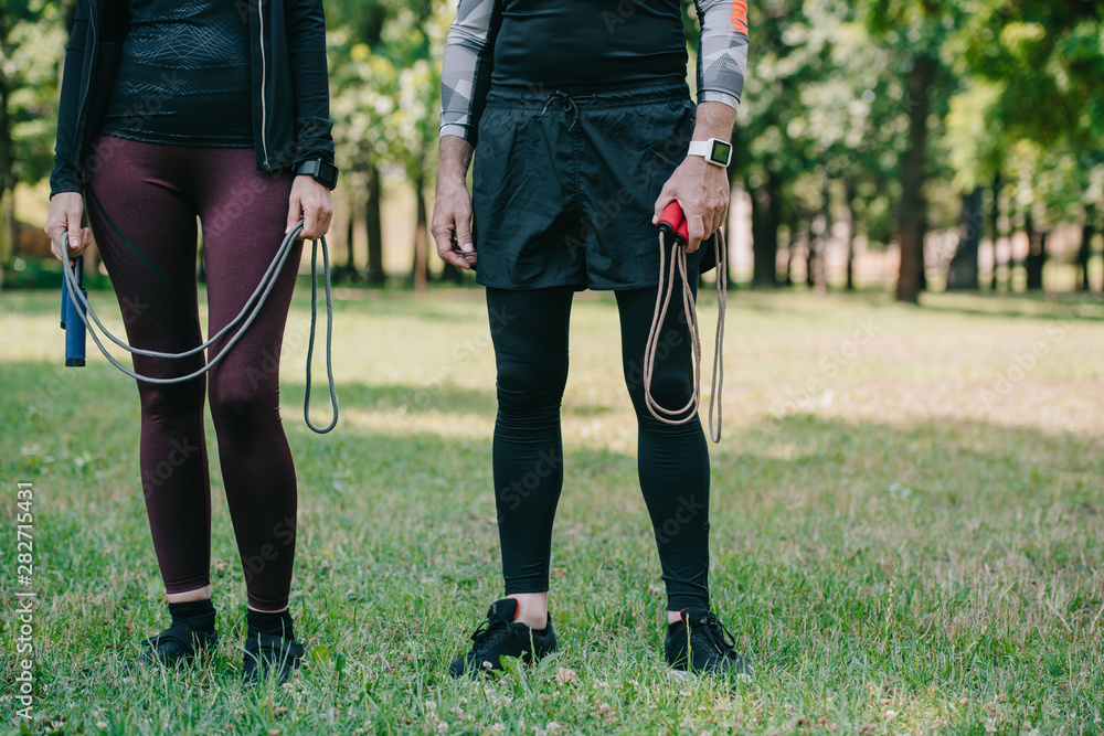 Fototapeta premium cropped view of mature sportsman and sportswoman holding jump ropes