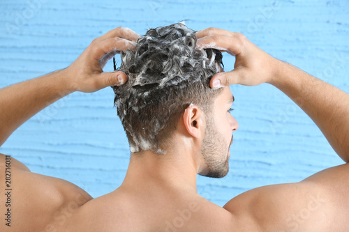 Handsome man washing hair on color background