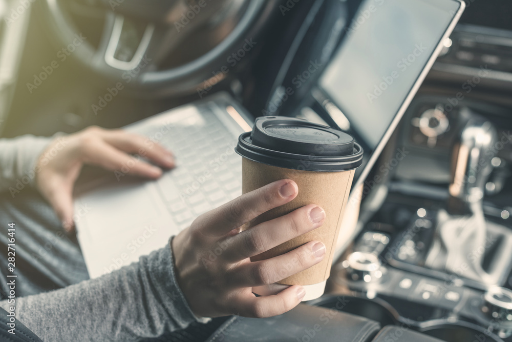 woman watching and using laptop while sitting on driver's seat in car and drinking coffee from paper cup. Crop image. Concept. woman watching and using laptop while sitting on driver's seat in car and drinking coffee from paper cup. Crop image. Concept.