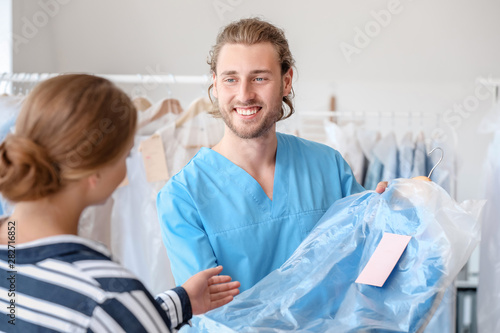 Male worker giving clothes to client in modern dry-cleaner's
