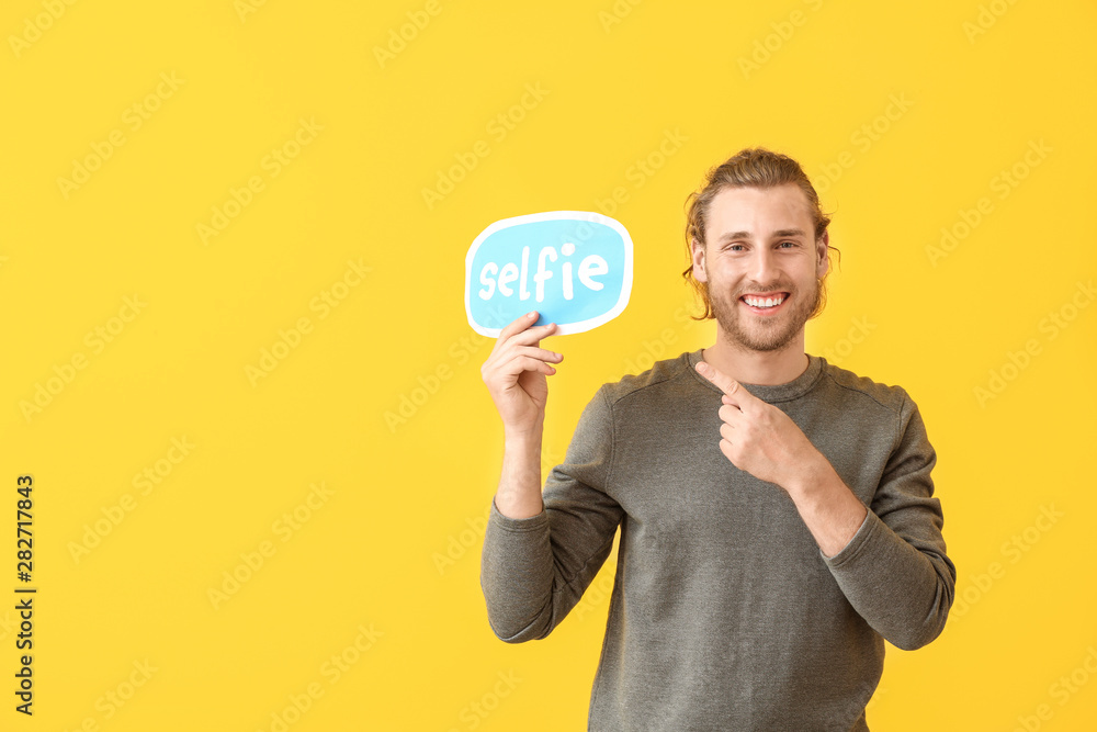 Male blogger holding paper with text SELFIE on color background - obrazy, fototapety, plakaty 
