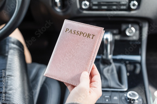 Border control concept. Woman holding passport in a pink cover sitting on driver's seat in car for check customs officers