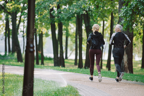 back view of mature, sportive runners jogging together in park
