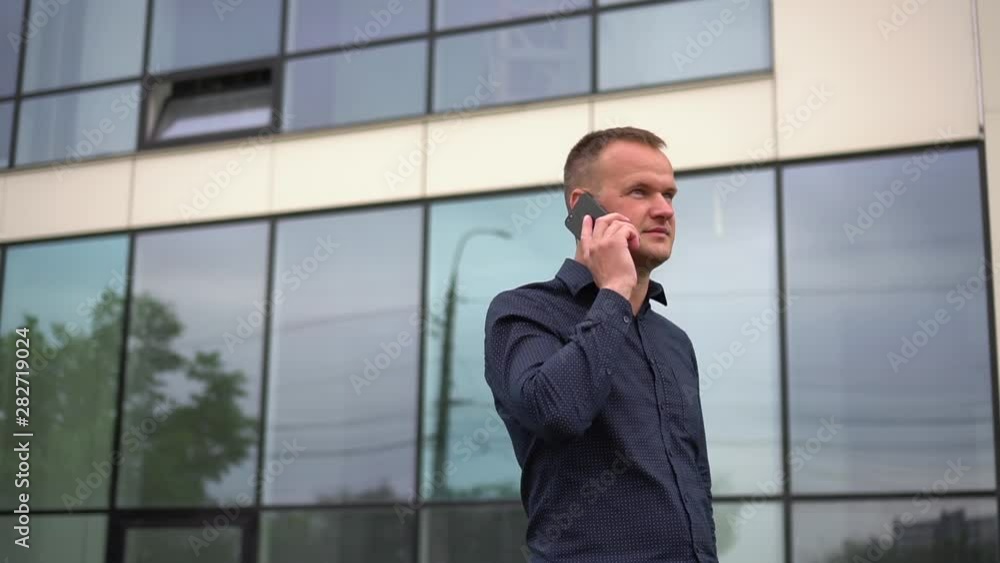 Handsome young guy walks at the business center and talks on the phone. Steady shot. Slow motion Handsome young guy walks at the business center and talks on the phone. Steady shot. Slow motion