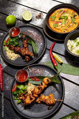 Asian dishes on a black table. Satay and Tom Yam