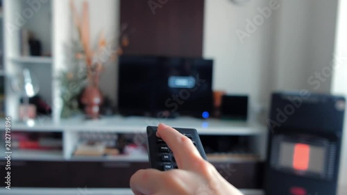 Close-up of female hand using TV remote control and switching channels on television.
