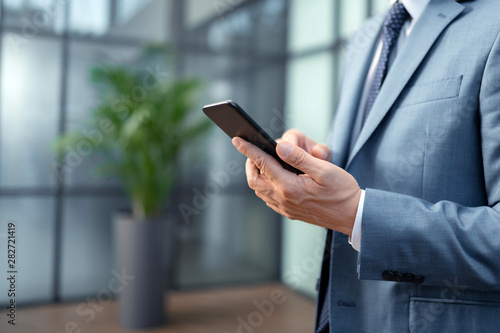 Close up of businessman wearing grey suit holding black smartphone