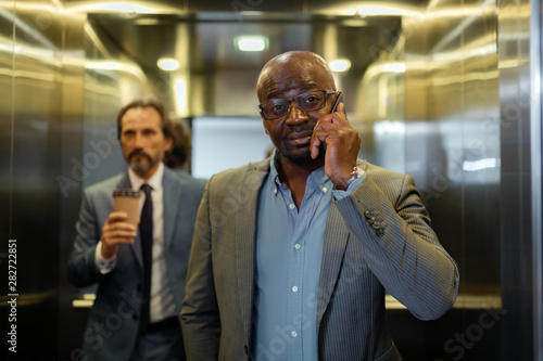 Dark-eyed businessman calling his colleague while standing in elevator