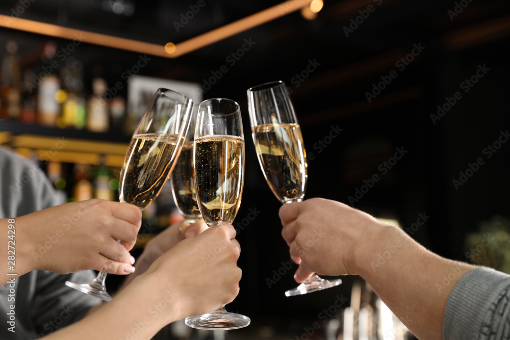 Friends clinking with glasses of champagne in bar, closeup
