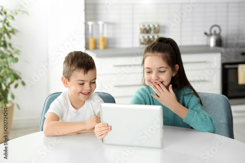 Little children using video chat on tablet at table in kitchen