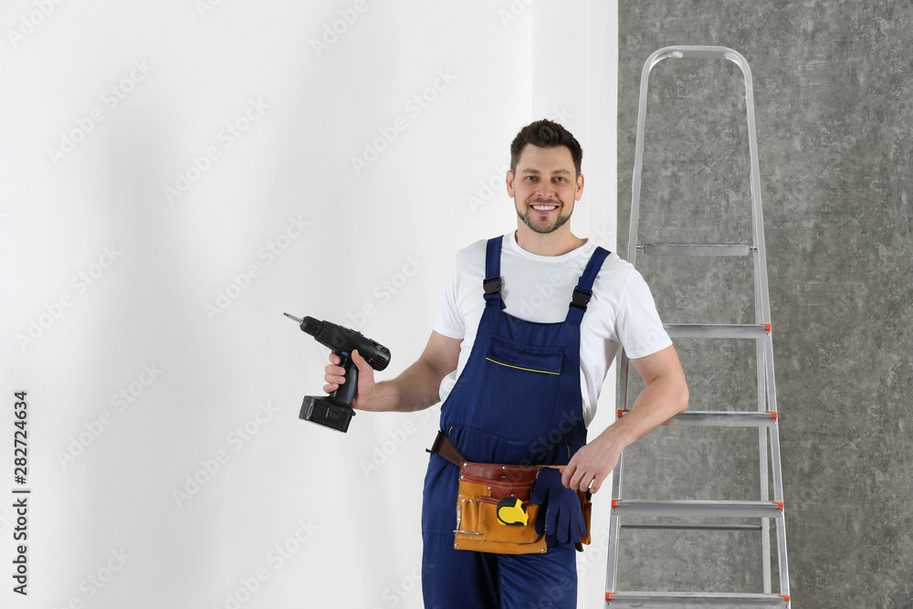 Handsome working man with electric screwdriver near wall. Home repair Handsome working man with electric screwdriver near wall. Home repair