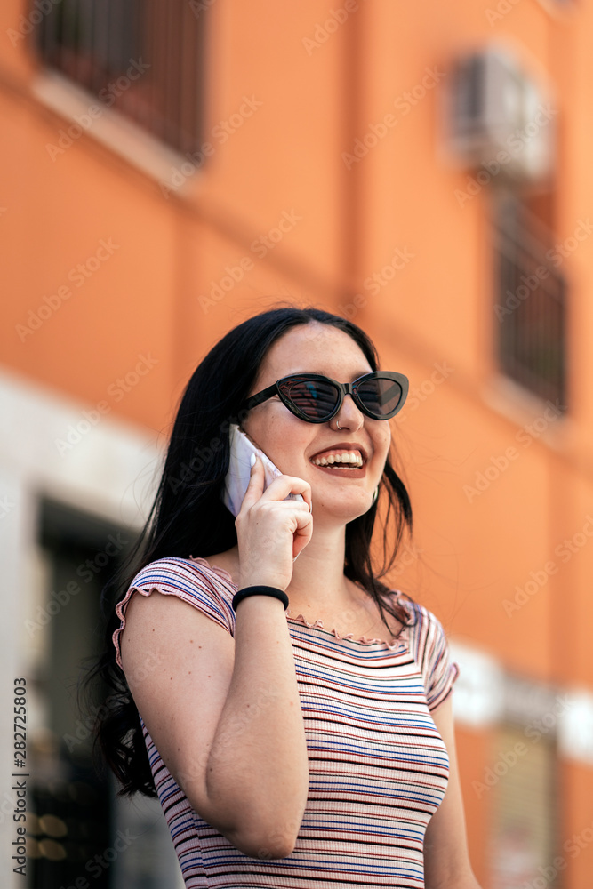 Urban smart casual pretty young woman talking on smartphone. Happy female adult speaking on mobile phone.