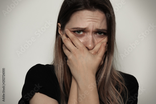 Scared woman covering mouth with her hands on light background. Stop violence