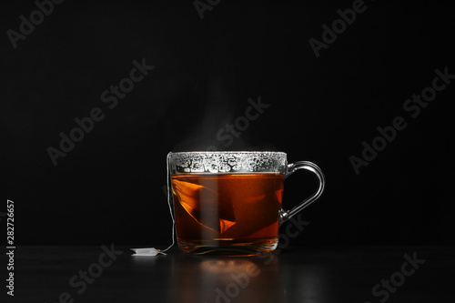 Glass cup of hot tea on table against black background, space for text