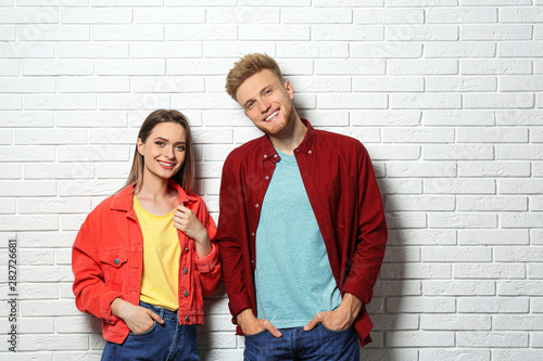 Young couple wearing blank t-shirts near white brick wall. Mockup for design