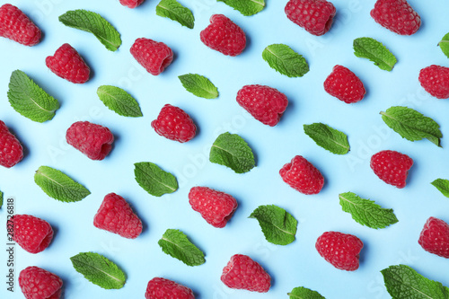 Flat lay composition with delicious ripe raspberries and leaves on blue background