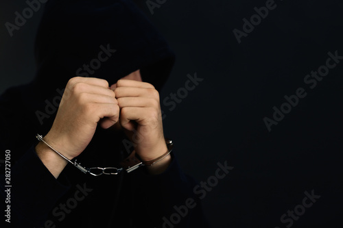 Man detained in handcuffs against dark background, space for text. Criminal law