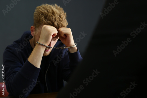 Police officer interrogating criminal in handcuffs indoors photo