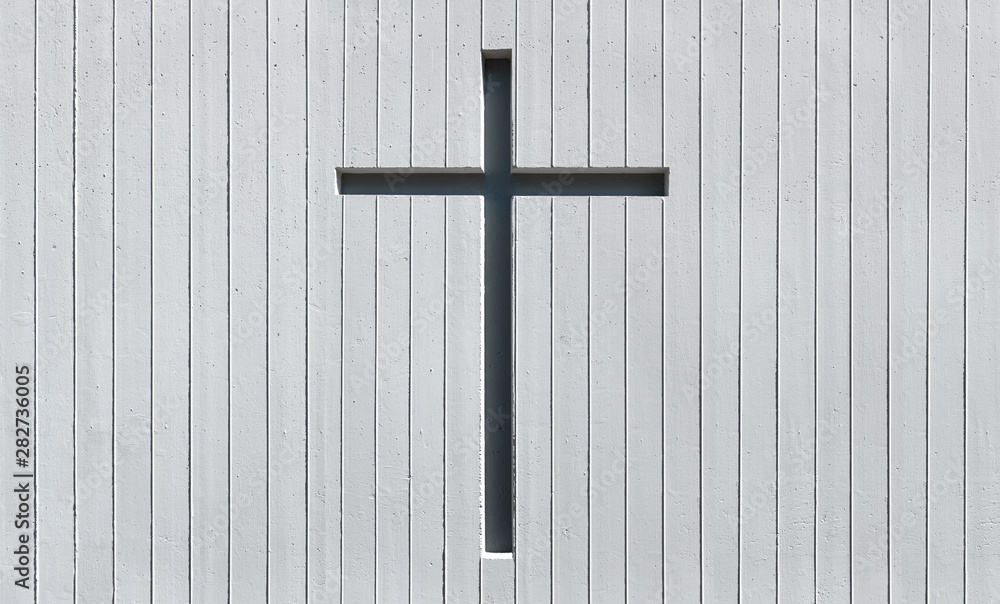 Kreuz in einer weißen Wand aus Sichtbeton mit vertikalem Streifenmuster