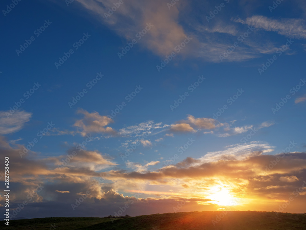 Cloudy sunset sky over a hill silhouette. Blue and orange color, Soft warm sun glow.