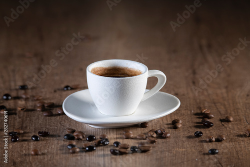 Top view of a white coffee cup surrounded by coffee seeds on a wooden table