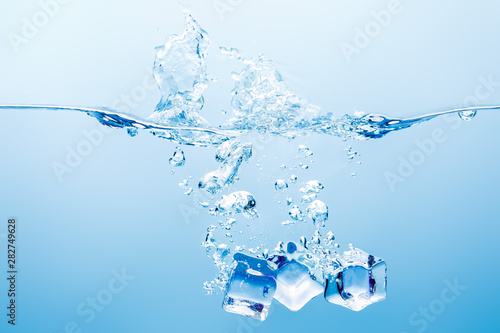 pure water with splash, bubbles and ice cubes on blue background
