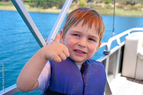 Cute little boy enjoying ride on a small boat. Little kid in the bow of a boat with his blue life jacket having fun. Travel adventure family vacation.