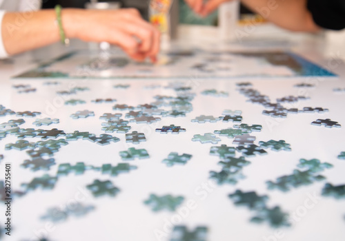 hands of two people putting together puzzles. focused and out-of-focus puzzle pieces in a white surface