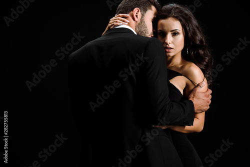 bearded man undressing attractive young woman isolated on black