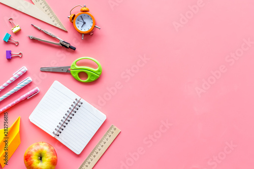 Back to school with stationary, notebook and alarm clock on pink student desk background top view mockup