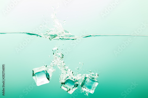transparent pure water with splash, ice cubes and bubbles on green background