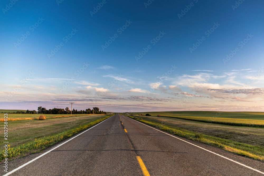 a long country highway rural highway road in North Dakota at sunset with a colorful sky