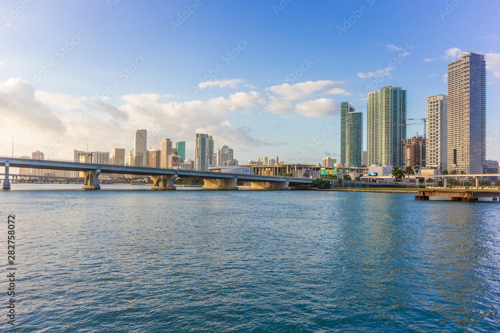 Miami city skyline panorama at blue sky cloudy with urban skyscrapers and bridge over sea with reflection